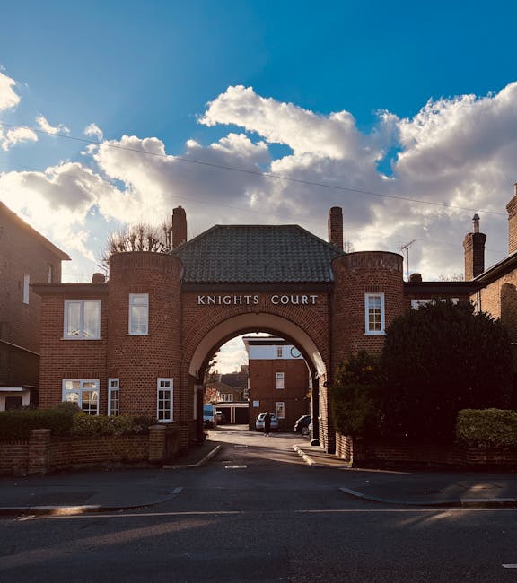 The image shows a brick residential building with an arched entrance labeled 'Knights Court,' featuring a tiled roof and multiple windows. The building is surrounded by a low brick wall and greenery, 