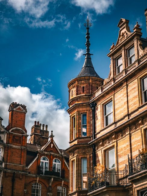 A row of Victorian-style terraced houses in Kingston upon Thames, featuring ornate white ironwork balconies, large bay windows, and decorative brickwork. The houses are set on a street with a brick re
